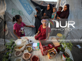 A displaced Palestinian girl is sitting on a stall selling biscuits, spices, and agricultural seedlings at a camp for displaced Palestinians...