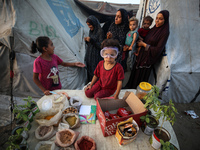 A displaced Palestinian girl is sitting on a stall selling biscuits, spices, and agricultural seedlings at a camp for displaced Palestinians...