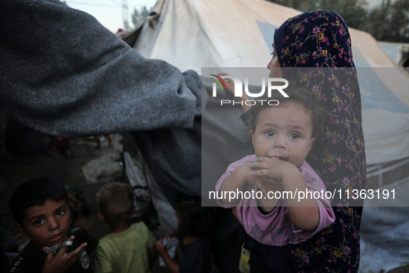 A displaced Palestinian woman is carrying her child at a camp for displaced Palestinians in Deir al-Balah, in the central Gaza Strip, on Jun...