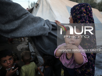 A displaced Palestinian woman is carrying her child at a camp for displaced Palestinians in Deir al-Balah, in the central Gaza Strip, on Jun...