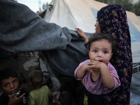 A displaced Palestinian woman is carrying her child at a camp for displaced Palestinians in Deir al-Balah, in the central Gaza Strip, on Jun...