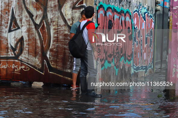 Two people are trying to cross a flooded street in the municipality of Nezahualcoyotl due to the heavy rains recorded yesterday, on June 27,...