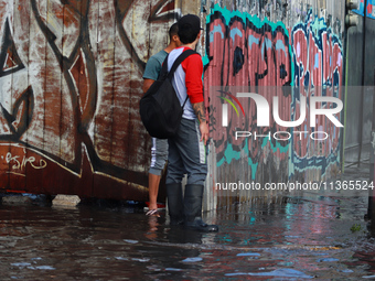 Two people are trying to cross a flooded street in the municipality of Nezahualcoyotl due to the heavy rains recorded yesterday, on June 27,...