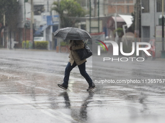 A woman is covering herself with an umbrella from the heavy rains on the Calzada Ermita south of the city, due to Tropical Wave Number 5, wh...