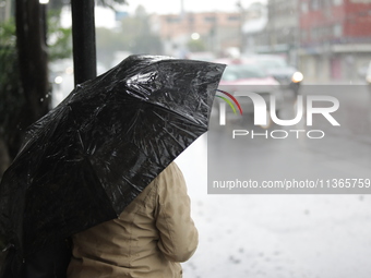 A woman is covering herself with an umbrella from the heavy rains on the Calzada Ermita south of the city, due to Tropical Wave Number 5, wh...