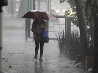 A woman is covering herself with an umbrella from the heavy rains on the Calzada Ermita south of the city, due to Tropical Wave Number 5, wh...