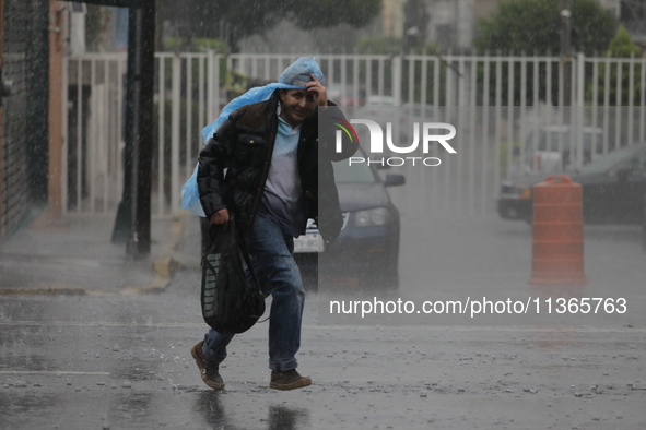 A man is wearing a waterproof to cover himself from the heavy rains on the Calzada Ermita south of the city, due to Tropical Wave Number 5,...