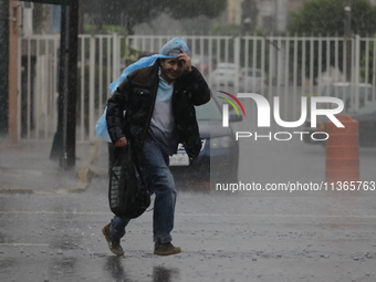 A man is wearing a waterproof to cover himself from the heavy rains on the Calzada Ermita south of the city, due to Tropical Wave Number 5,...