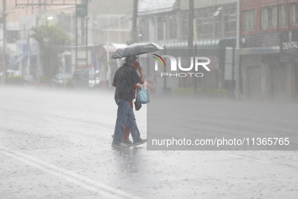 A couple is covering themselves with an umbrella from the heavy rains on the Calzada Ermita south of the city, due to Tropical Wave Number 5...