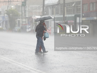 A couple is covering themselves with an umbrella from the heavy rains on the Calzada Ermita south of the city, due to Tropical Wave Number 5...