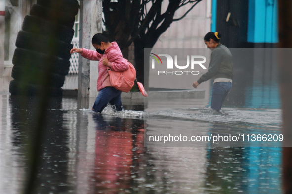 Women are walking with their legs submerged in the water, trying to cross Vicente Villada Avenue, which is flooded due to the heavy rains th...