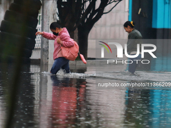 Women are walking with their legs submerged in the water, trying to cross Vicente Villada Avenue, which is flooded due to the heavy rains th...