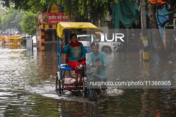 A man is pushing his cycle rickshaw with a passenger through a flooded street after heavy rains in New Delhi, India, on June 28, 2024. 