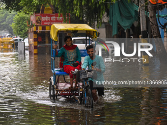 A man is pushing his cycle rickshaw with a passenger through a flooded street after heavy rains in New Delhi, India, on June 28, 2024. (