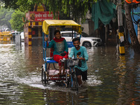 A man is pushing his cycle rickshaw with a passenger through a flooded street after heavy rains in New Delhi, India, on June 28, 2024. (