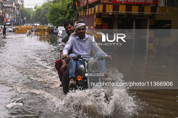 A man is riding his bike through a flooded street after heavy rains in New Delhi, India, on June 28, 2024. 