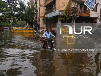 A food delivery person is riding his electric bike through a flooded street after heavy rains in New Delhi, India, on June 28, 2024. (