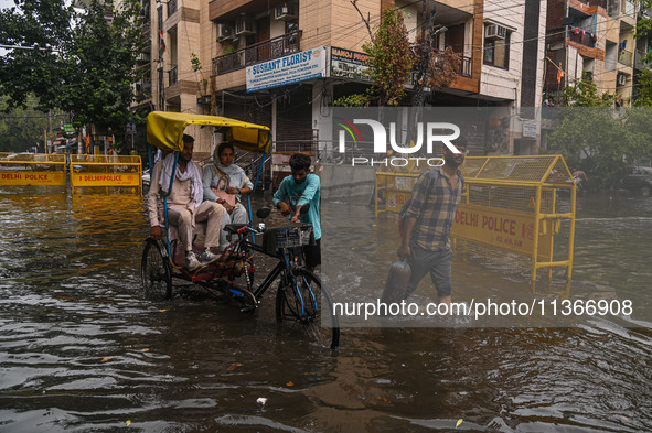 People are wading through a flooded street after heavy rains in New Delhi, India, on June 28, 2024. 