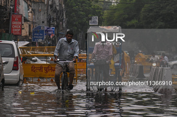 People are wading through a flooded street after heavy rains in New Delhi, India, on June 28, 2024. 