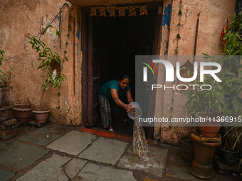 Unnati Prakash, 42, is throwing water with the help of a bucket outside her house that is flooded with water after heavy rains in New Delhi,...