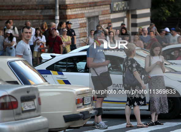 People are standing by a police car during a search and rescue effort at an apartment block hit by a Russian missile in Dnipro, Ukraine, on...