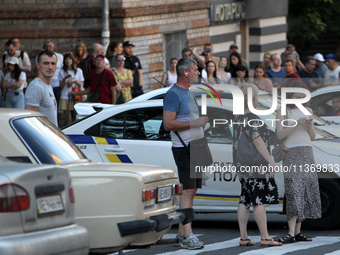 People are standing by a police car during a search and rescue effort at an apartment block hit by a Russian missile in Dnipro, Ukraine, on...