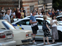 People are standing by a police car during a search and rescue effort at an apartment block hit by a Russian missile in Dnipro, Ukraine, on...