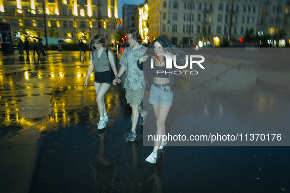 Young people are seen walking during a downpour in Warsaw, Poland on 28 June, 2024. 