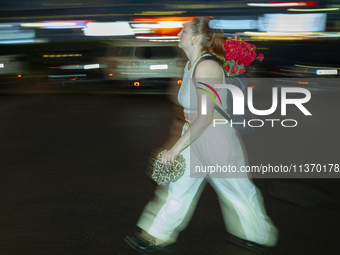 A woman with a bouquet of flowers in her backpack is seen during a downpour in Warsaw, Poland on 28 June, 2024. (