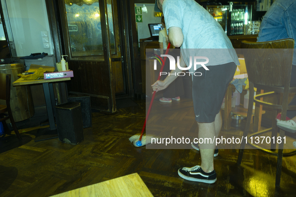 A man is seen sweeping a floor in a restaurant after a downpour in Warsaw, Poland on 28 June, 2024. 