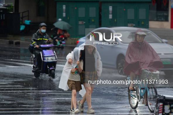 A mother is walking with her daughter, who is covered with a raincoat, in stormy weather in Shanghai, China, on June 30, 2024. 