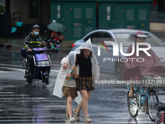 A mother is walking with her daughter, who is covered with a raincoat, in stormy weather in Shanghai, China, on June 30, 2024. (