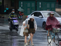 A mother is walking with her daughter, who is covered with a raincoat, in stormy weather in Shanghai, China, on June 30, 2024. (