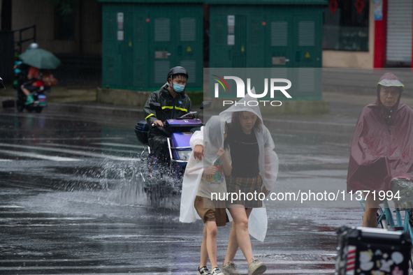 A mother is walking with her daughter, who is covered with a raincoat, in stormy weather in Shanghai, China, on June 30, 2024. 