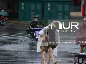 A mother is walking with her daughter, who is covered with a raincoat, in stormy weather in Shanghai, China, on June 30, 2024. (