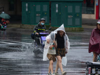 A mother is walking with her daughter, who is covered with a raincoat, in stormy weather in Shanghai, China, on June 30, 2024. (