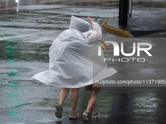 A mother is walking with her daughter, who is covered with a raincoat, in stormy weather in Shanghai, China, on June 30, 2024. (