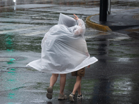 A mother is walking with her daughter, who is covered with a raincoat, in stormy weather in Shanghai, China, on June 30, 2024. (