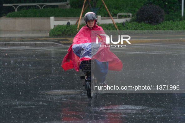 A woman is riding a motor scooter in stormy weather in Shanghai, China, on June 30, 2024. 