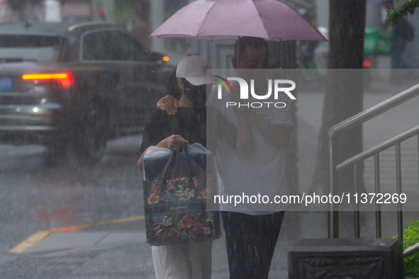 A couple is struggling with an umbrella in stormy weather in Shanghai, China, on June 30, 2024. 