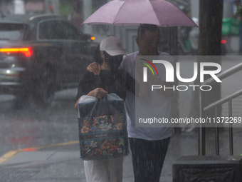 A couple is struggling with an umbrella in stormy weather in Shanghai, China, on June 30, 2024. (