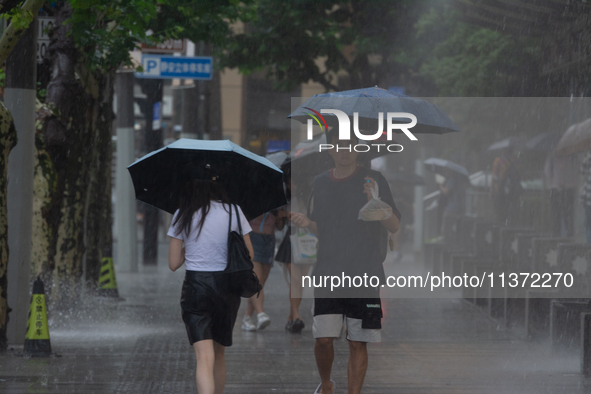 People are walking with umbrellas under heavy rain in stormy weather in Shanghai, China, on June 30, 2024. 