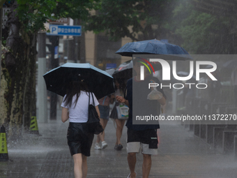 People are walking with umbrellas under heavy rain in stormy weather in Shanghai, China, on June 30, 2024. (