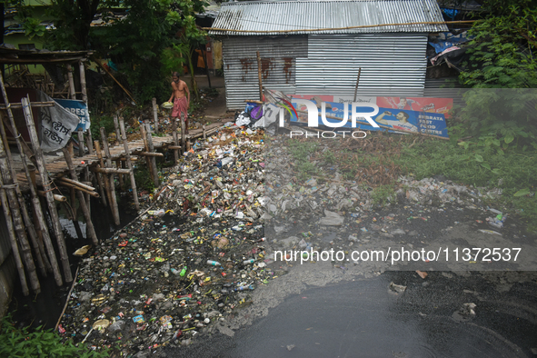 A person is passing a canal full of plastic waste on the outskirts of Kolkata, India, on June 30, 2024. 