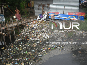 A person is passing a canal full of plastic waste on the outskirts of Kolkata, India, on June 30, 2024. (