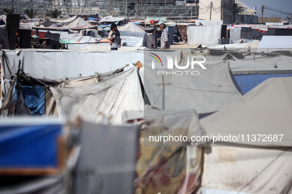 Palestinians are walking along an alley between tents sheltering displaced Palestinians in Rafah in the southern Gaza Strip on June 30, 2024...