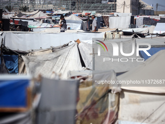 Palestinians are walking along an alley between tents sheltering displaced Palestinians in Rafah in the southern Gaza Strip on June 30, 2024...