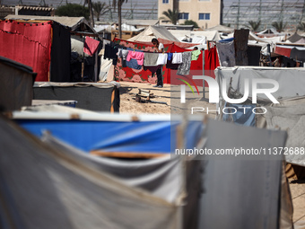 Palestinians are walking along an alley between tents sheltering displaced Palestinians in Rafah in the southern Gaza Strip on June 30, 2024...