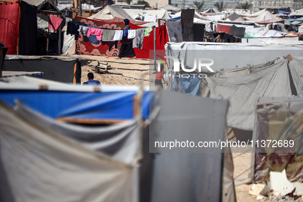 Palestinians are walking along an alley between tents sheltering displaced Palestinians in Rafah in the southern Gaza Strip on June 30, 2024...