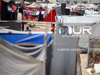 Palestinians are walking along an alley between tents sheltering displaced Palestinians in Rafah in the southern Gaza Strip on June 30, 2024...